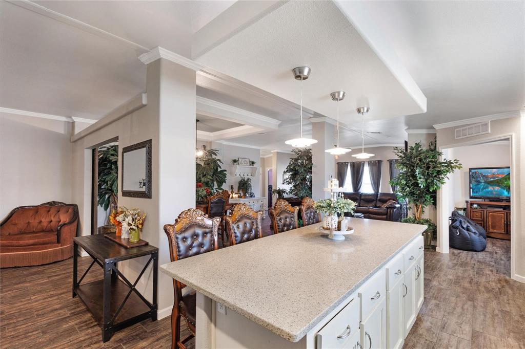 Bright, spacious living area featuring a large kitchen island with white cabinetry, elegant wooden chairs, plush seating, and vibrant greenery, exuding a warm, inviting vibe.