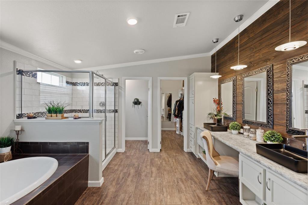 Spacious modern bathroom with wood accents, featuring a large tub and glass shower. Double vanity with decorative mirrors and a cozy seating area.