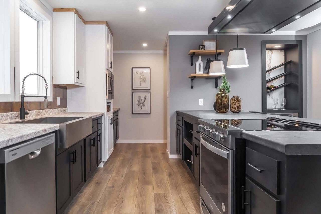 Modern kitchen with light wood flooring, contrasting black and white cabinets, and stainless-steel appliances. Shelves hold decorative items, creating a sleek, elegant vibe.