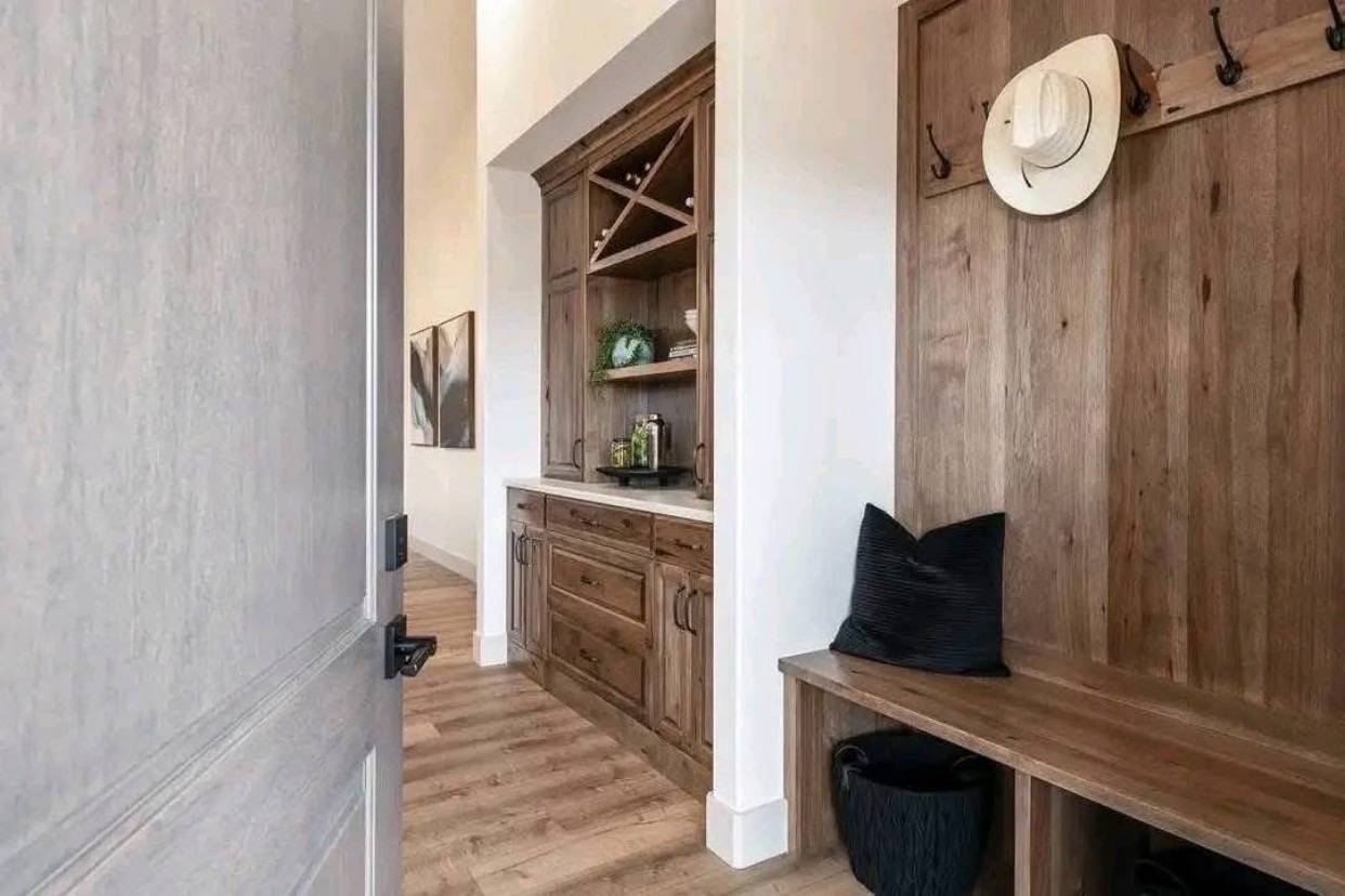 Cozy mudroom with wooden cabinetry and bench. A white hat hangs on the wall, and a black pillow sits on the bench, enhancing the rustic decor.