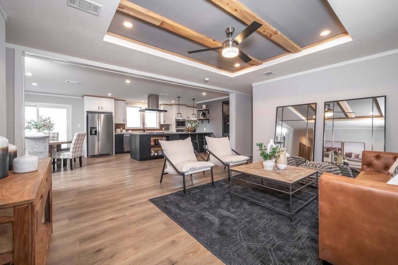 Modern living room and kitchen with open layout. Features include wood floors, leather couch, sleek furniture, ceiling fan, and ample lighting.