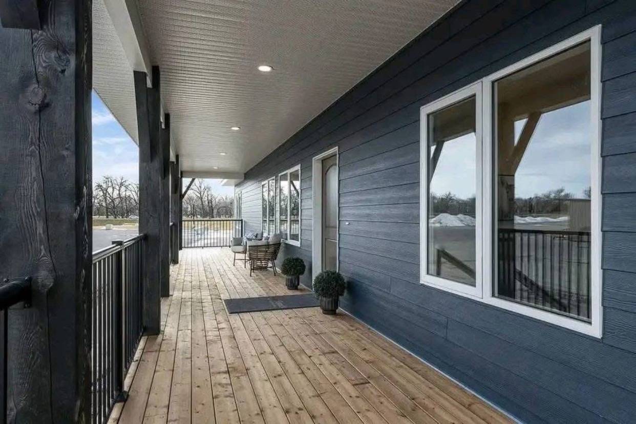 Spacious wooden porch with a modern design features a dark blue exterior, large windows, potted plants, and outdoor seating, evoking a calm, inviting atmosphere.