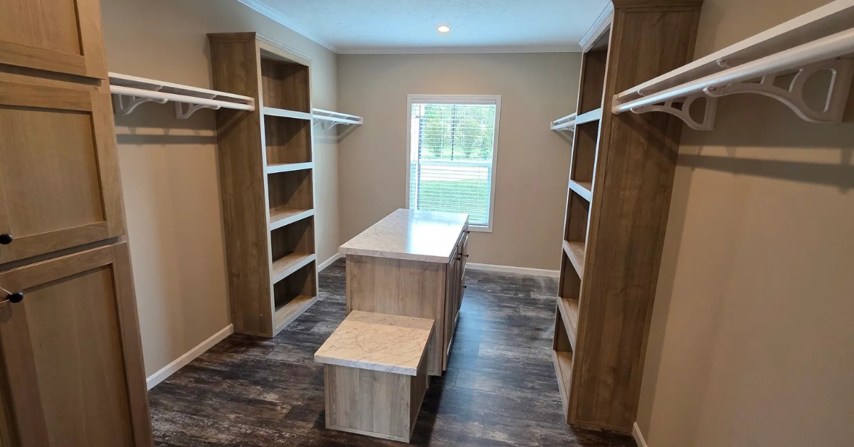 Spacious walk-in closet with wooden shelves, central island, and clothes racks. Light streams through a window, highlighting the modern, organized space.