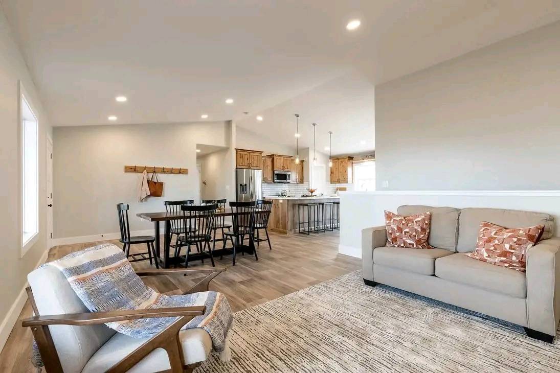Open-concept living space with a cozy beige sofa and patterned pillows, a wooden armchair, modern dining area, and a sleek kitchen with pendant lighting.