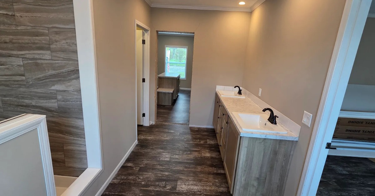 Modern bathroom with dual sinks on a wooden vanity, textured beige walls, and wood-patterned flooring. Bright lighting and a walk-in shower on the left.