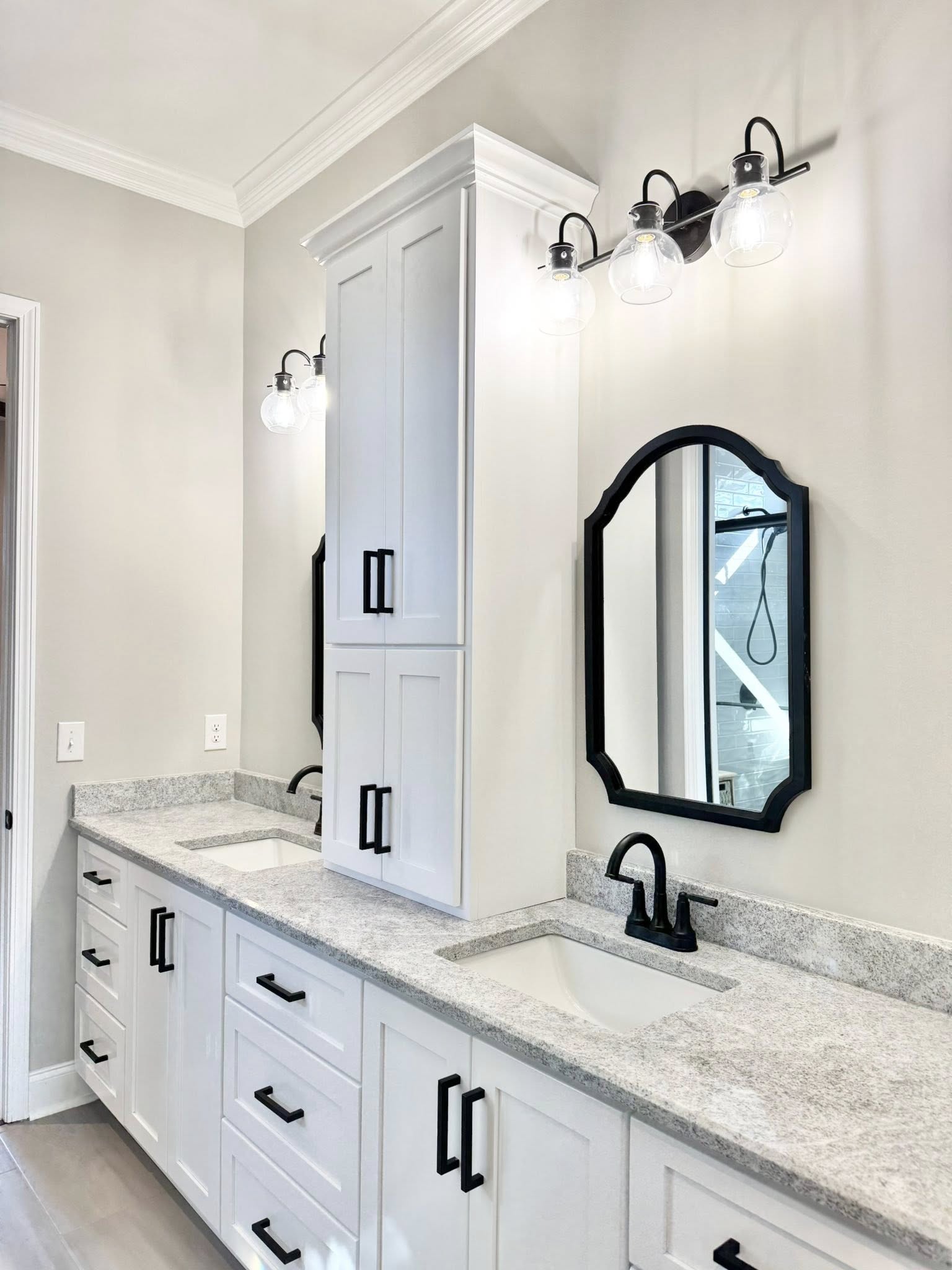 Elegant bathroom with dual white vanities, granite countertop, and two black-edged mirrors. Wall-mounted lights create a bright, modern feel.