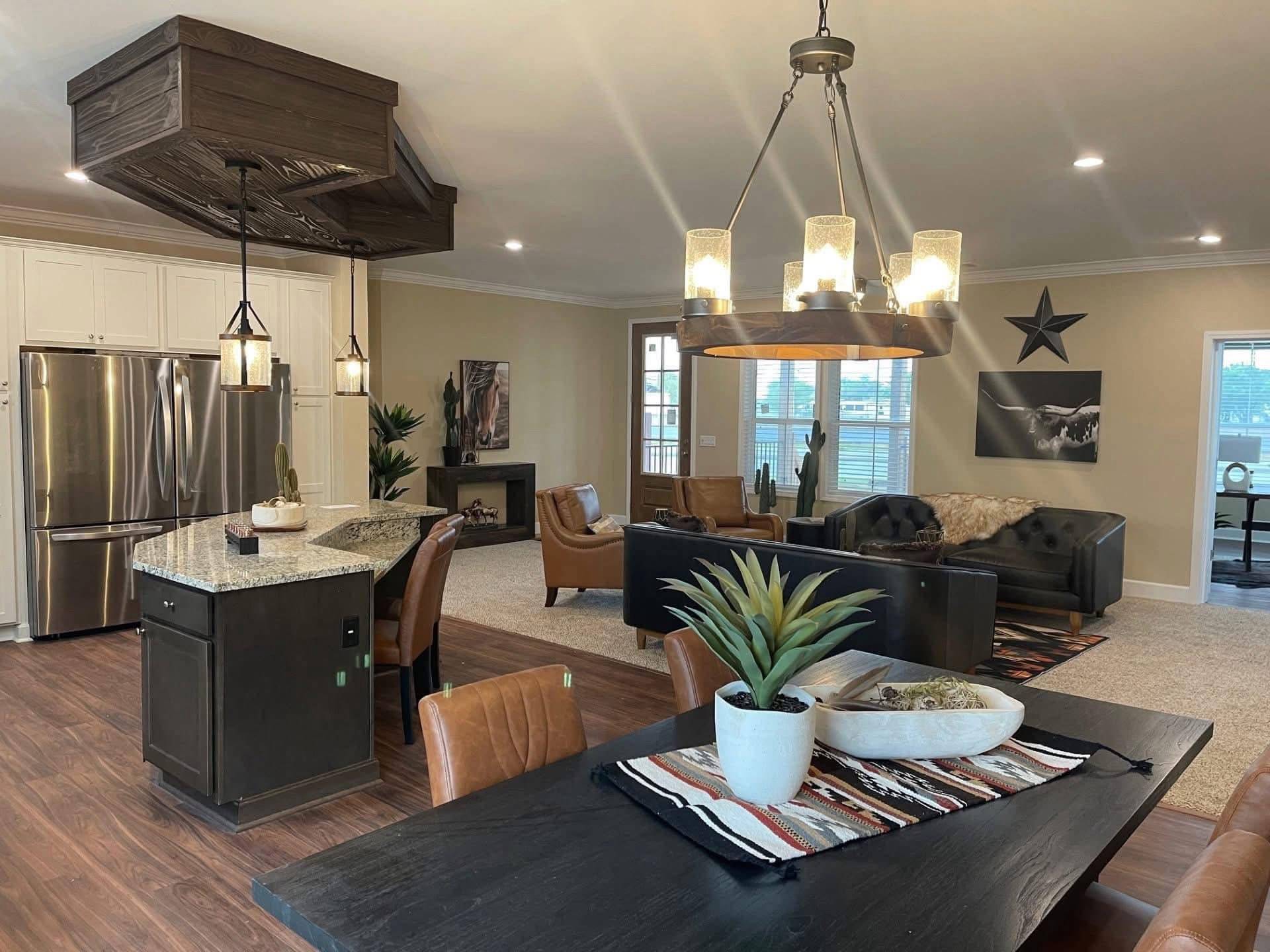 Open-plan living room and kitchen with warm lighting. Features leather sofas, modern furniture, a decorative star on the wall, and a centerpiece plant.