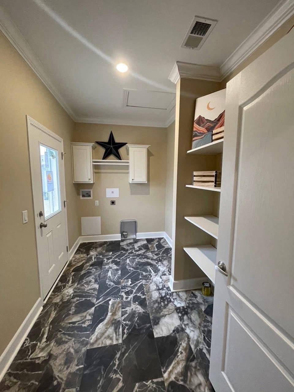 A laundry room with black and white marble-patterned floor tiles, cream walls, and white cabinetry. A black star decorates the wall above the cabinets, and shelves hold decorative items. A door with a window is on the left. The room has a clean and modern feel.
