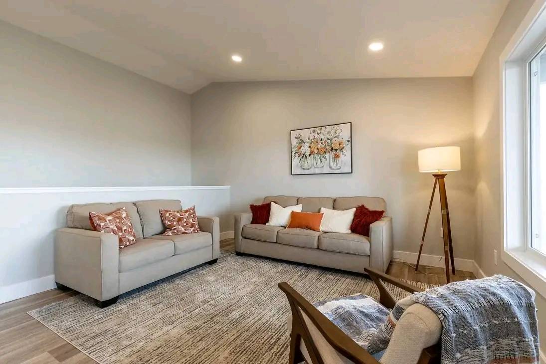 Modern living room with beige sofas adorned with colorful cushions, a floral painting, wooden floor lamp, and a cozy chair with a blanket, creating a warm atmosphere.