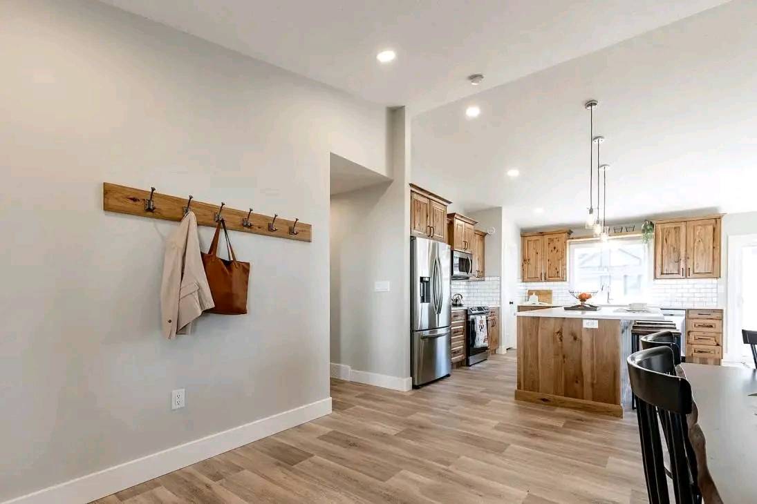 Bright, modern kitchen with wooden floors, cabinets, and island. Stainless steel appliances and pendant lights create a cozy, warm atmosphere. Coatrack with a jacket and bag on the left wall.