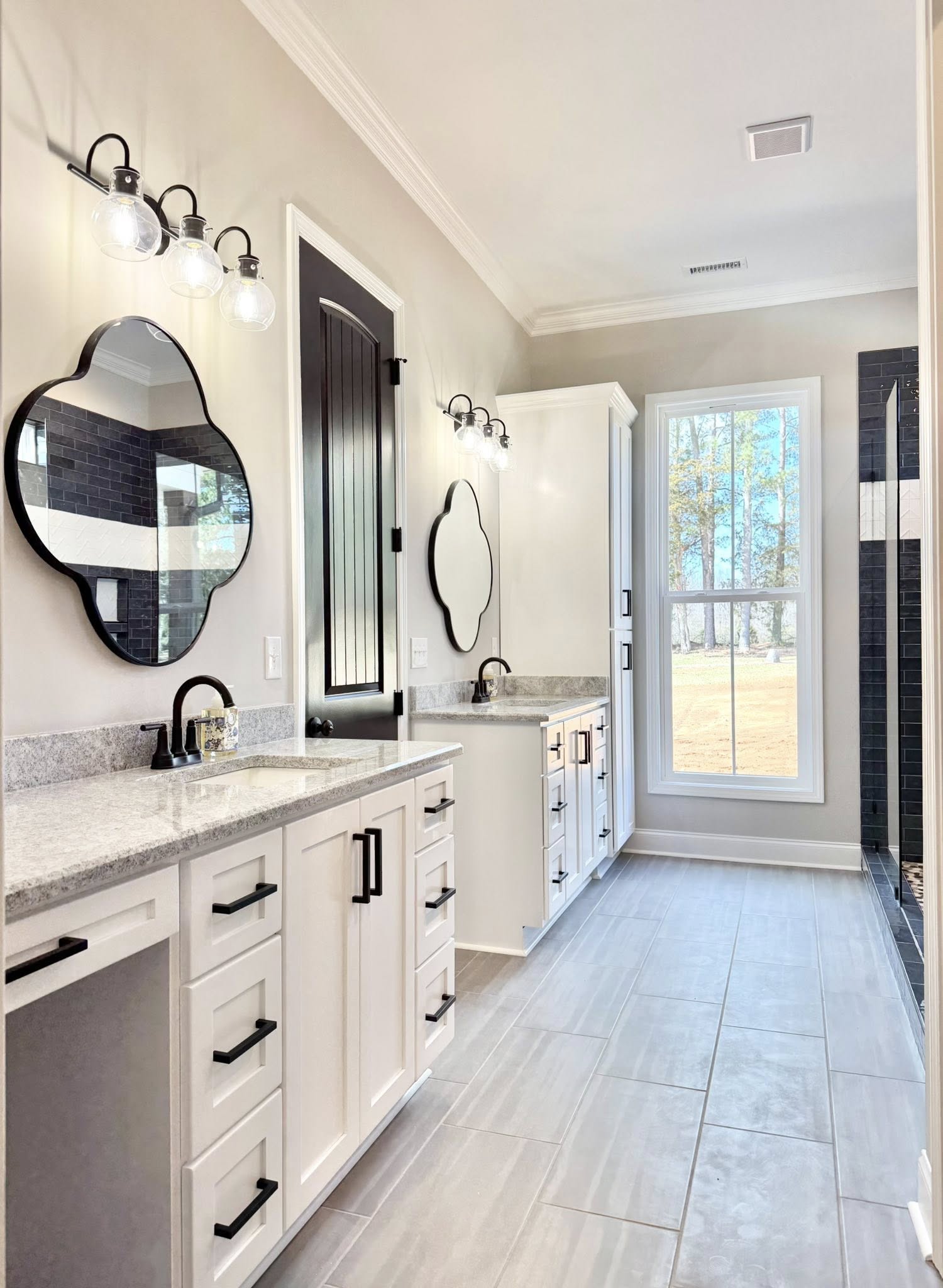 A modern bathroom with a white toilet and vanity. Black faucet and handles complement the gray countertop. An elegant mirror and light fixture add a classic touch.