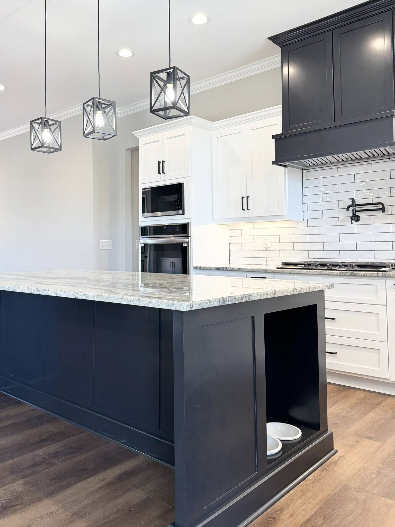 Modern kitchen with a sleek black island featuring a marble countertop. White cabinets, stainless steel appliances, and pendant lights add elegance.