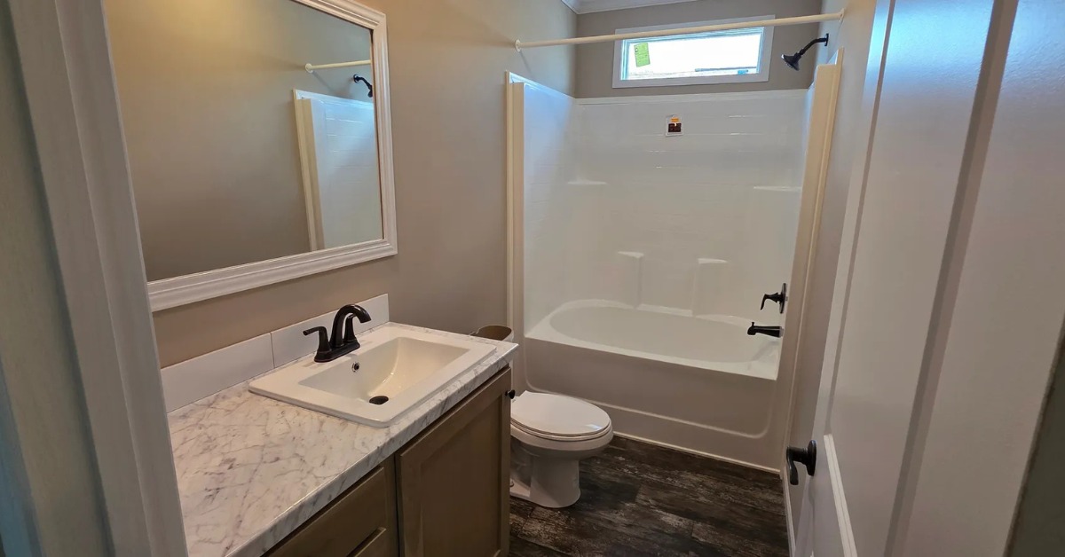 A modern bathroom with a marble countertop, white sink, and black faucet. Includes a toilet, white bathtub, and a large mirror, under soft lighting.