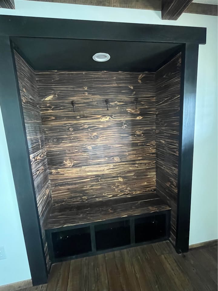 Nook with dark wood paneling, two hooks on the back wall, small seat, and cubbies beneath. Overhead light and cozy, rustic feel.