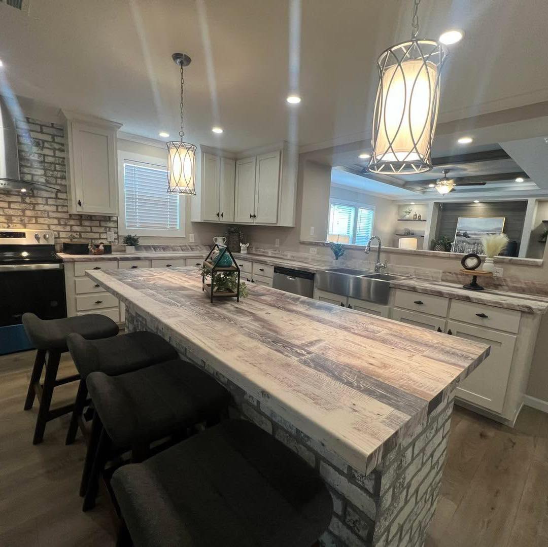 A modern kitchen with a rustic wood island, surrounded by four black stools. Pendant lights hang above. White cabinets and a stainless steel oven and sink add contrast, creating a warm, inviting atmosphere.