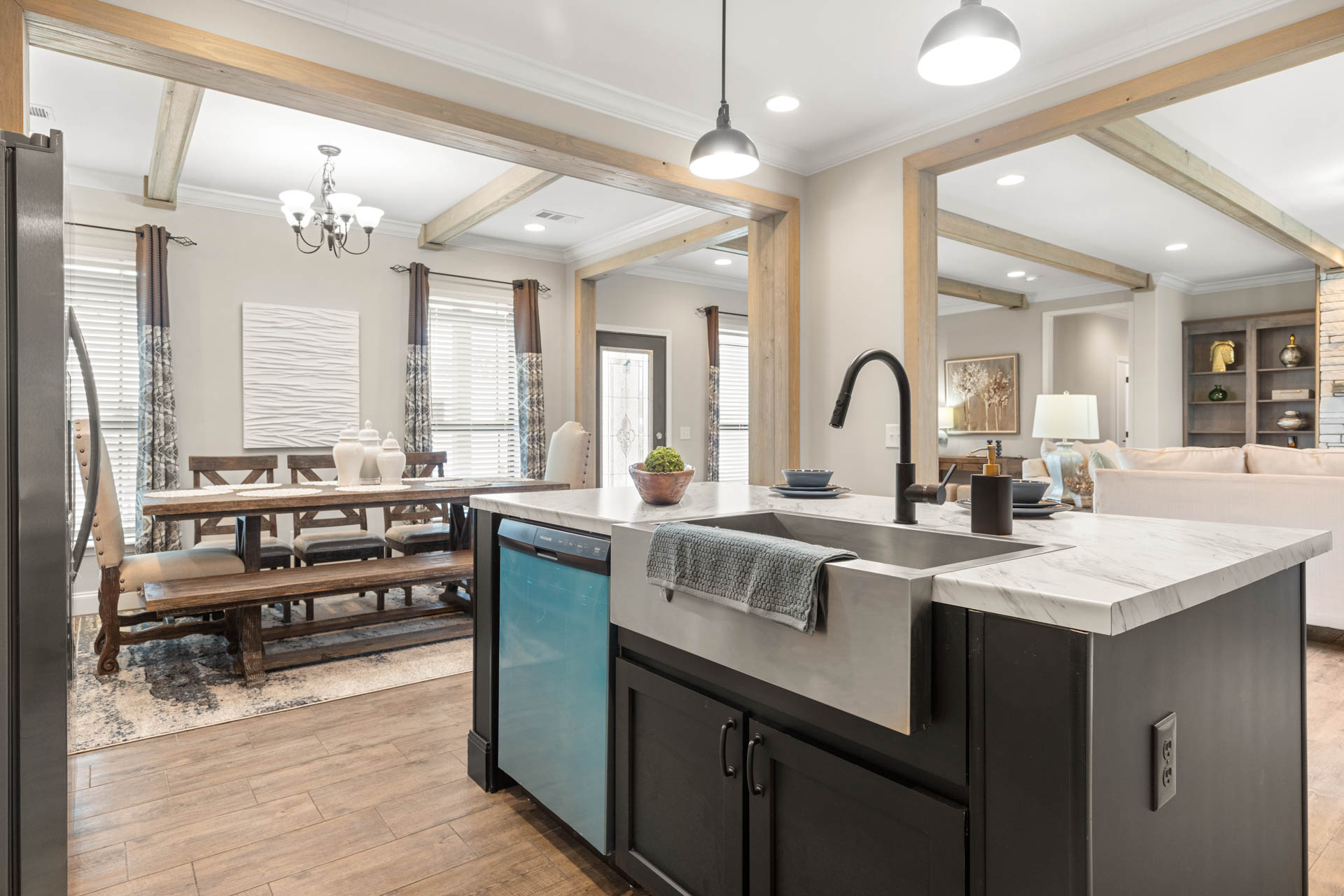 Open-concept kitchen and dining area with a modern farmhouse vibe. Features a large island with a sink, wooden beams, a dining table, and soft lighting.