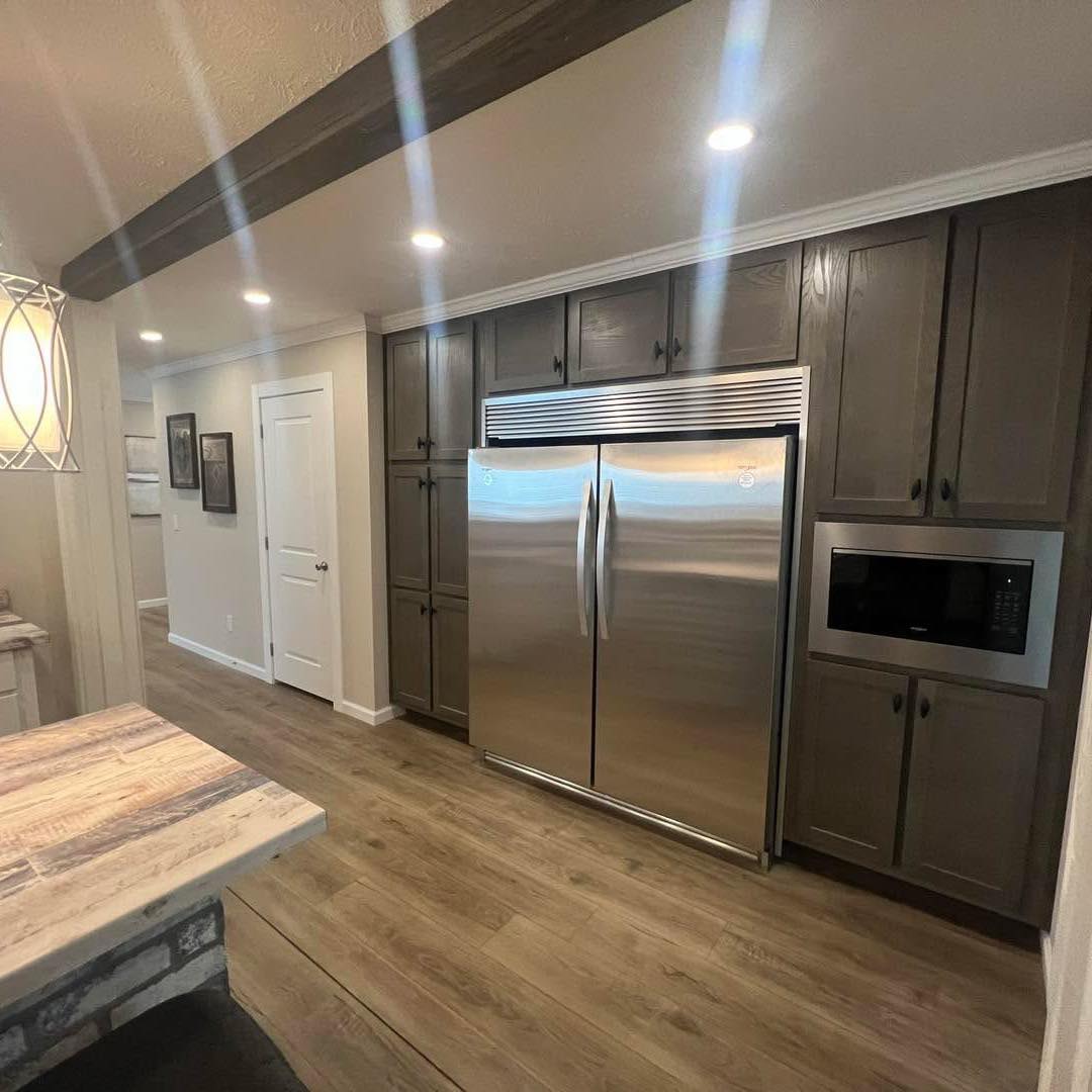 Modern kitchen with a large stainless steel fridge, dark wood cabinets, and a built-in microwave. The warm lighting and wooden floor create a cozy atmosphere.