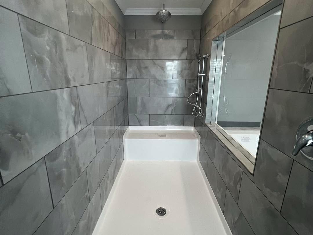 Modern bathroom with gray marble-patterned tile walls and a white floor. Features a large mirror, sleek silver fixtures, and a serene, clean ambiance.
