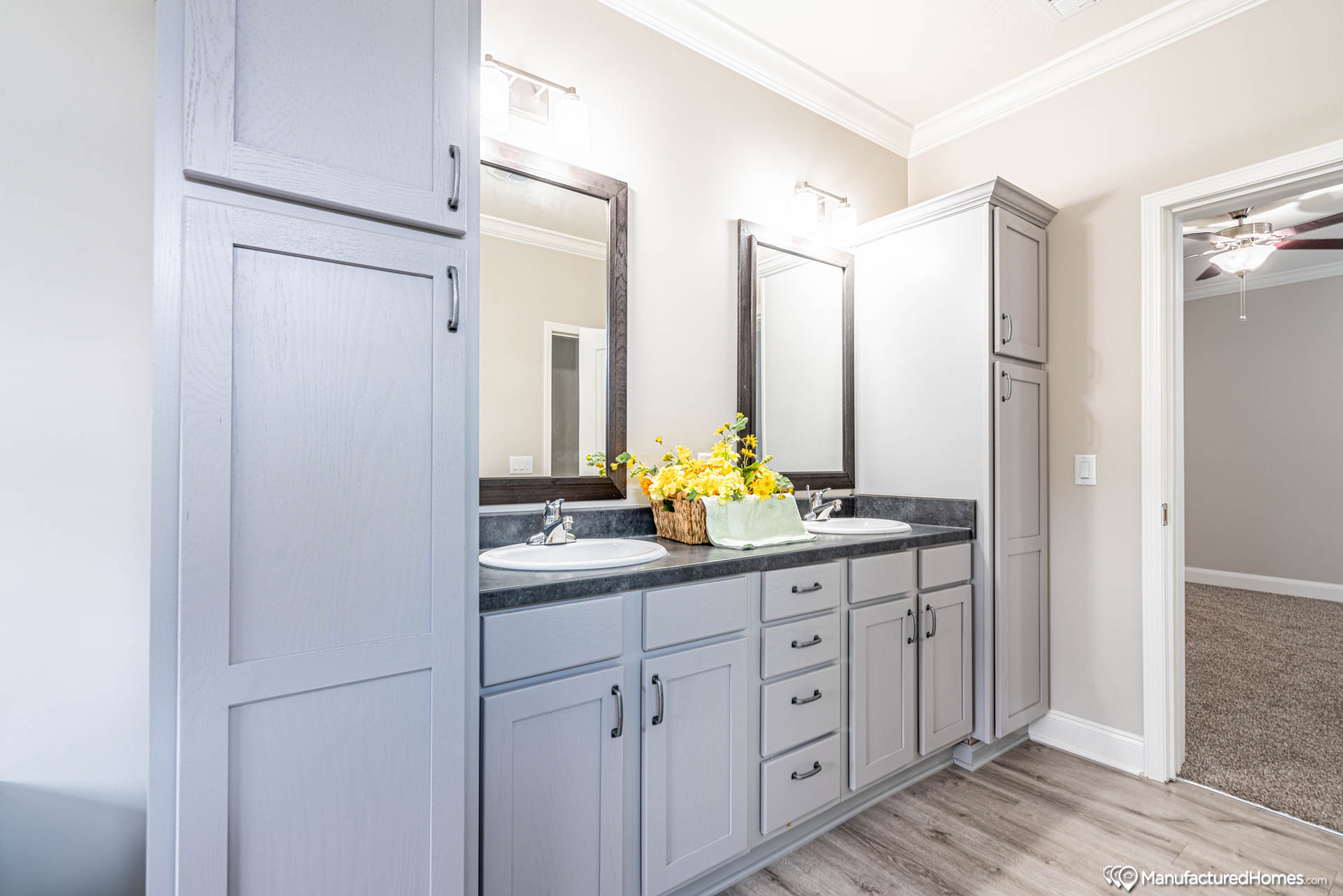 Modern bathroom with light gray cabinets, double sinks, and large mirrors. A cheerful bouquet of yellow flowers sits on the counter, adding brightness.