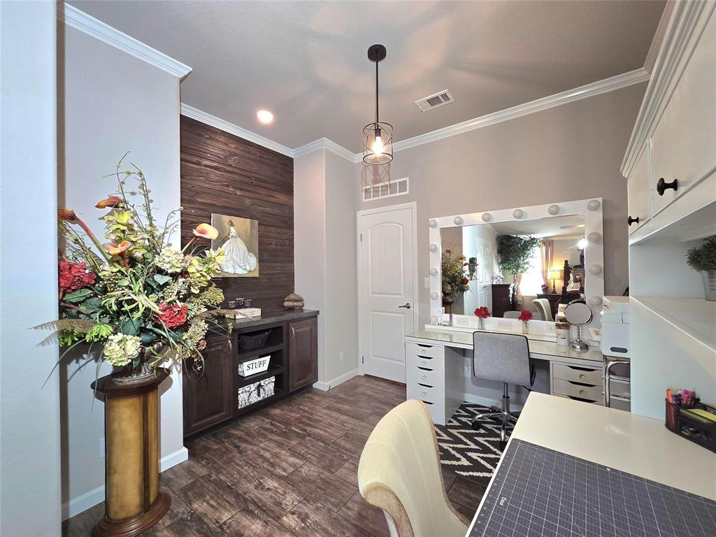 Cozy office with a wood accent wall and vanity desk featuring round lights. It includes a tall floral arrangement and stylish chair on wooden flooring.