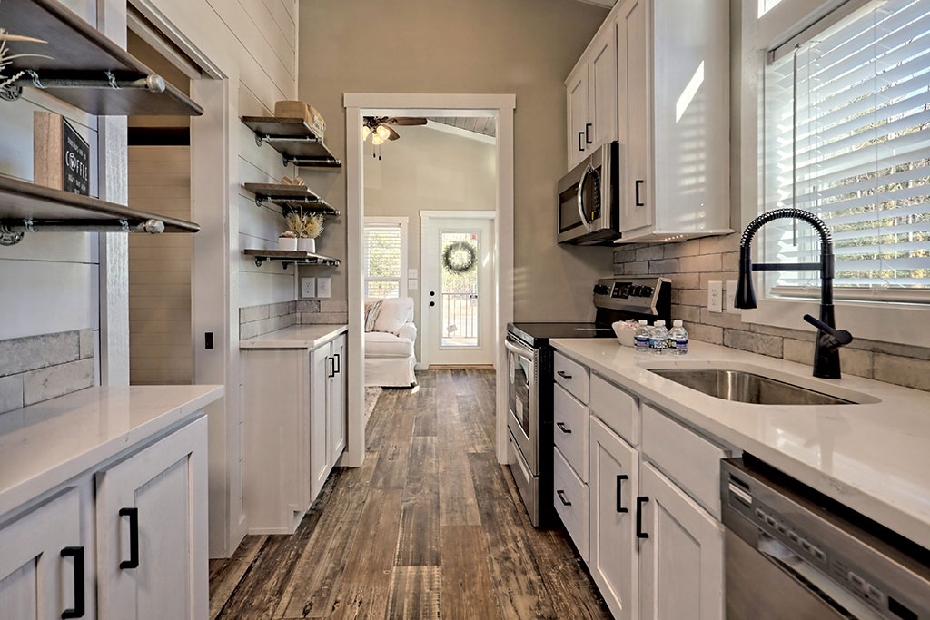 Sleek kitchen with white cabinets, stainless steel appliances, and dark wood floors. Sunlight streams through a window, creating a cozy ambiance.