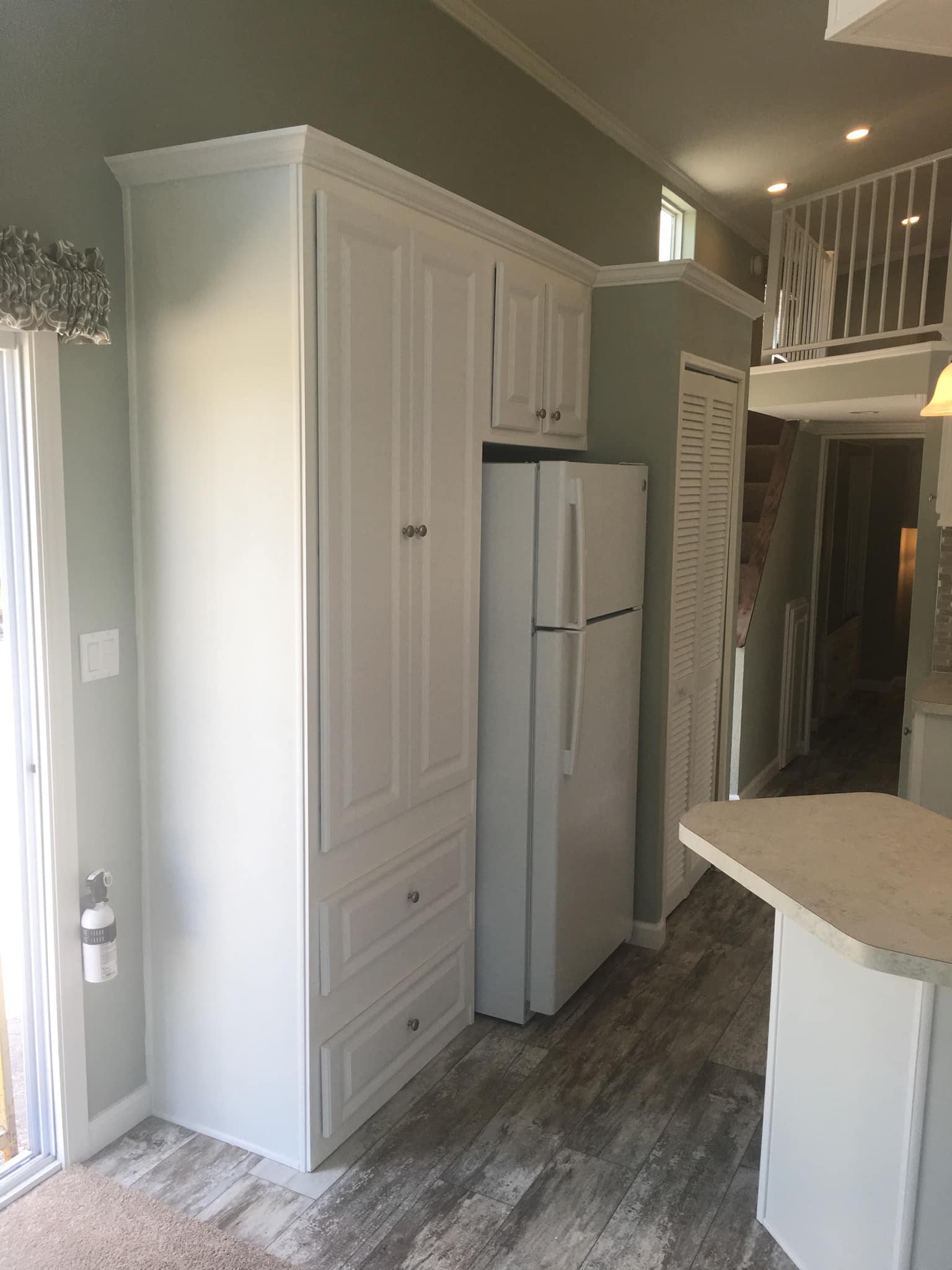 Compact kitchen with a white fridge, matching cabinets, and light wood flooring. A small staircase leads to an upper level, creating a cozy tone.