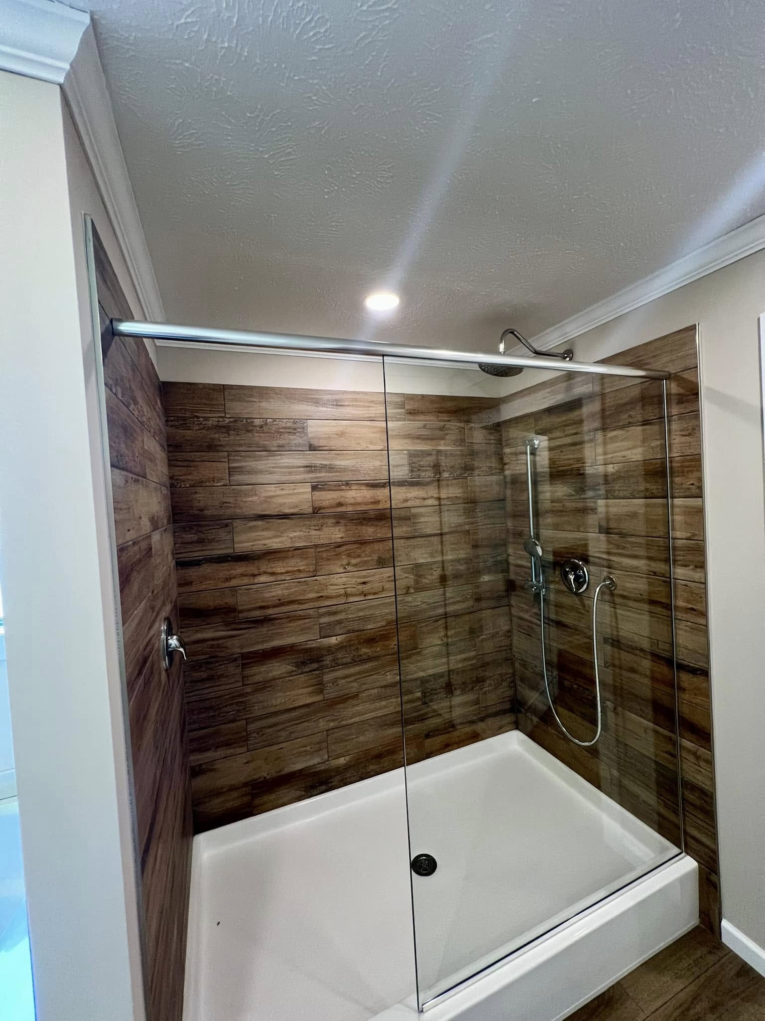 Modern bathroom with a glass-enclosed shower featuring wood-patterned tiles. Overhead lighting highlights the spacious, clean design.