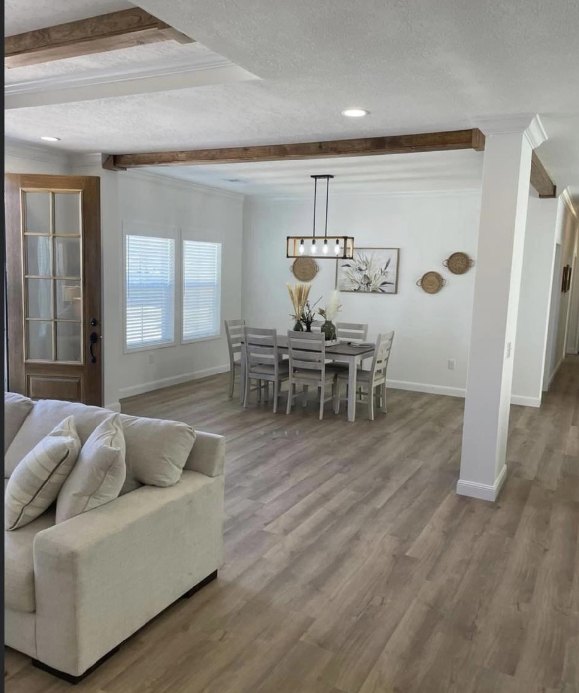 Modern dining room with a wooden table and six chairs, a pendant light, and wall decor. Light wood floors and a beige couch create a cozy atmosphere.