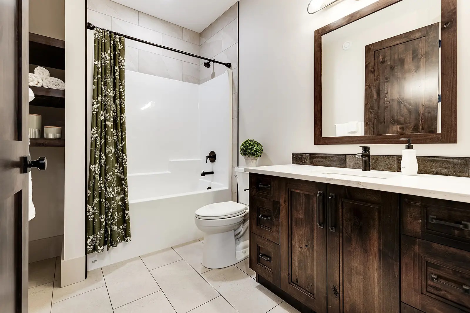 Stylish bathroom with a dark wood vanity, large mirror, and white sink. Green floral shower curtain, white tub, and neatly folded towels on shelves.