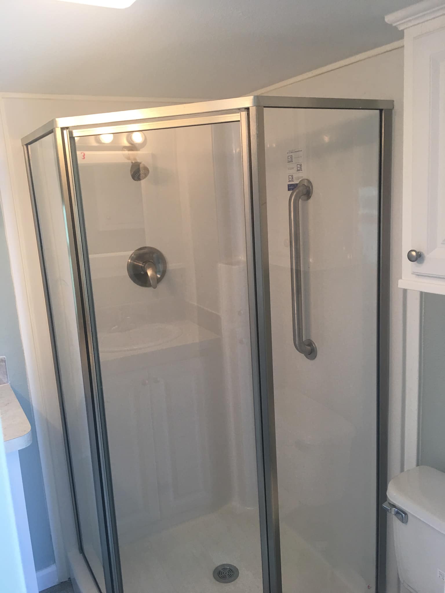Small bathroom with a glass shower enclosure that has a metal frame and grab bar. The shower has a silver faucet and is adjacent to a white cabinet.