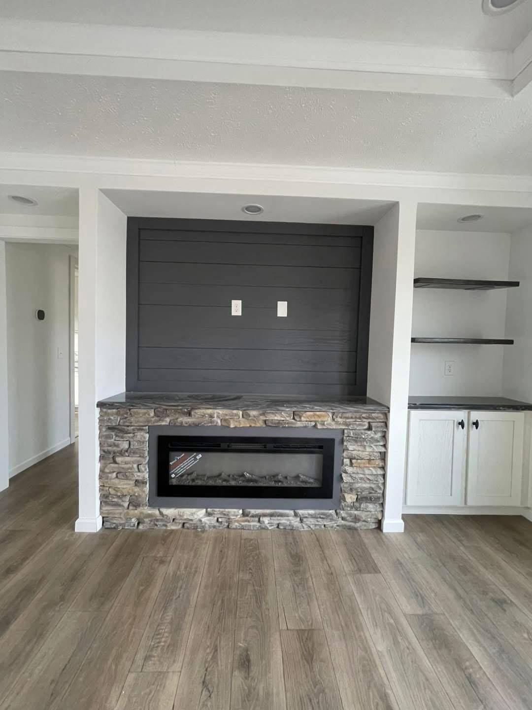 Modern living room with a stone fireplace set into a shiplap accent wall. Natural wood flooring and white built-in shelves create a cozy, inviting atmosphere.