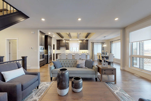 Spacious modern living room with a gray sofa, blue accents, and large windows. Open-plan kitchen and dining area with wooden floors and contemporary decor. Cozy and inviting atmosphere.