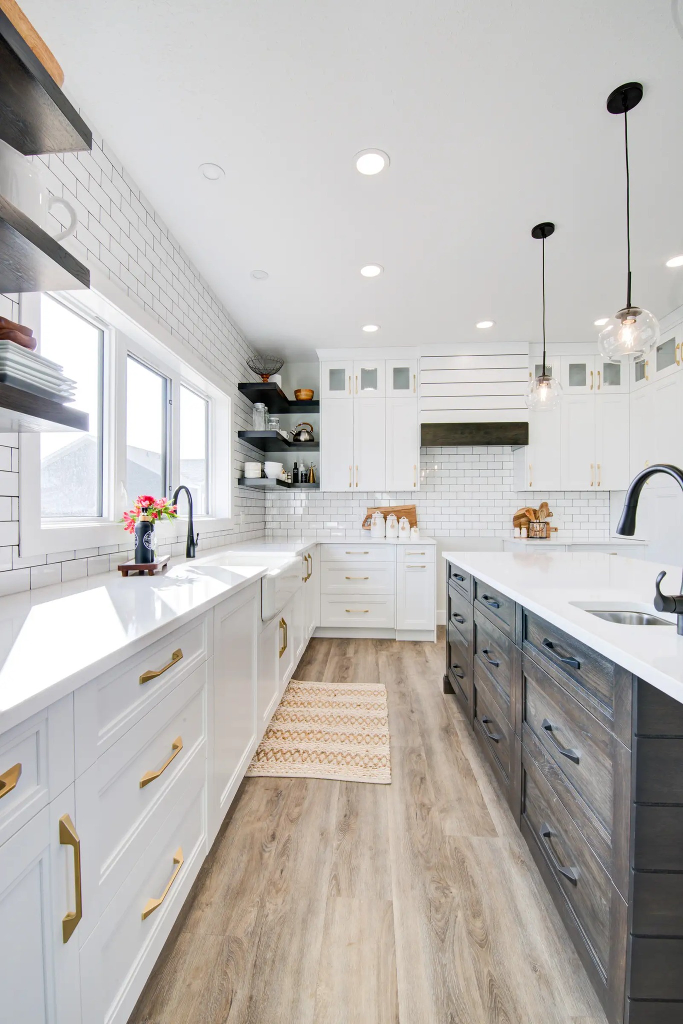 Bright kitchen with white cabinets, light wood floors, and black accents. Features large windows, pendant lights, and open shelving. Clean and modern.