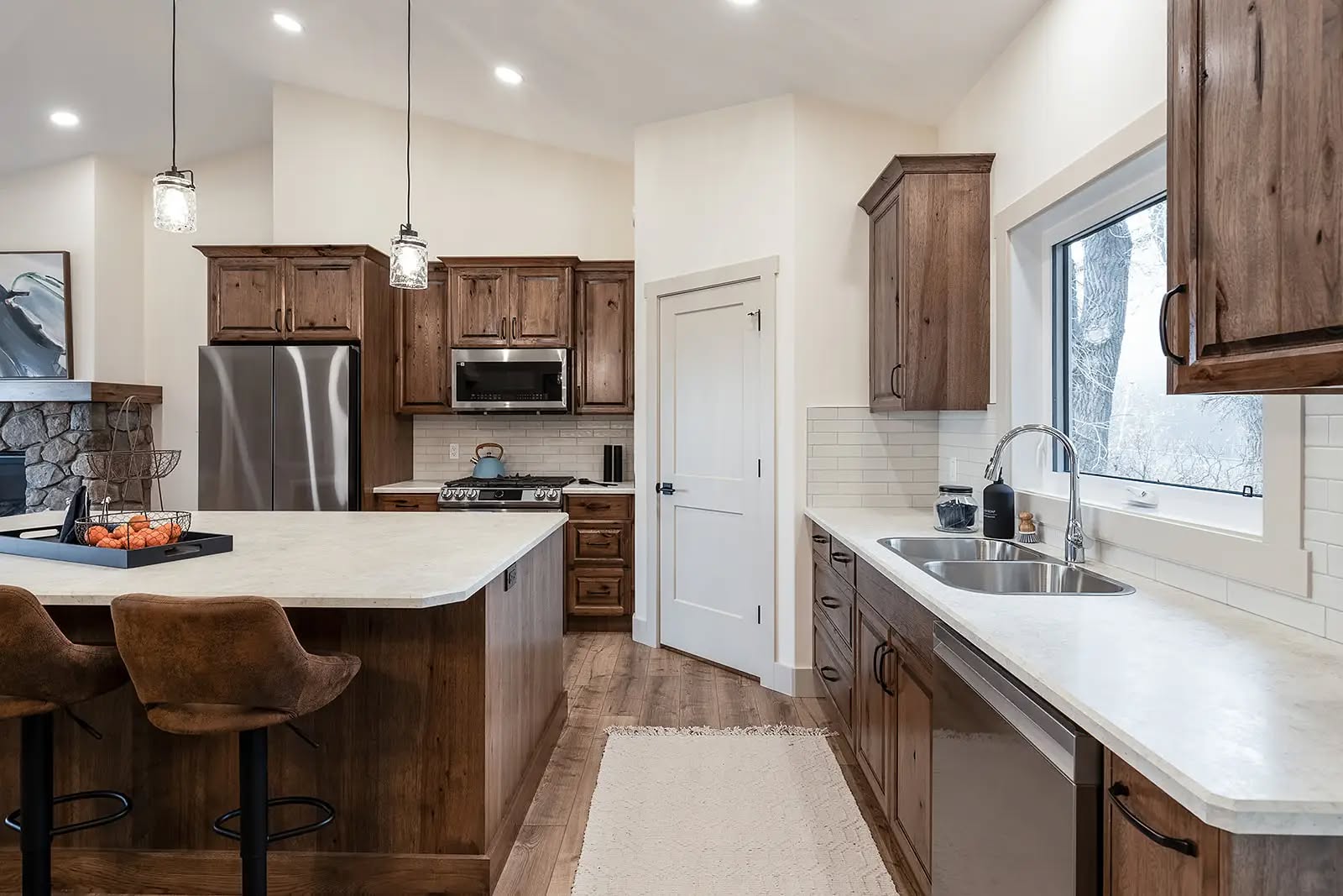 Modern kitchen with wooden cabinets, a large island with bar stools, stainless steel appliances, and pendant lights. Bright, inviting atmosphere.