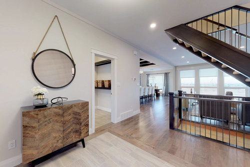 Modern open-concept interior with wooden floors, a spiral staircase, and large windows. A round mirror and side table add elegance near the entrance.