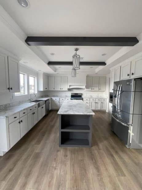 Spacious kitchen with white cabinets, marble countertops, and stainless steel appliances. Central island, modern lighting, and wood flooring create a sleek look.