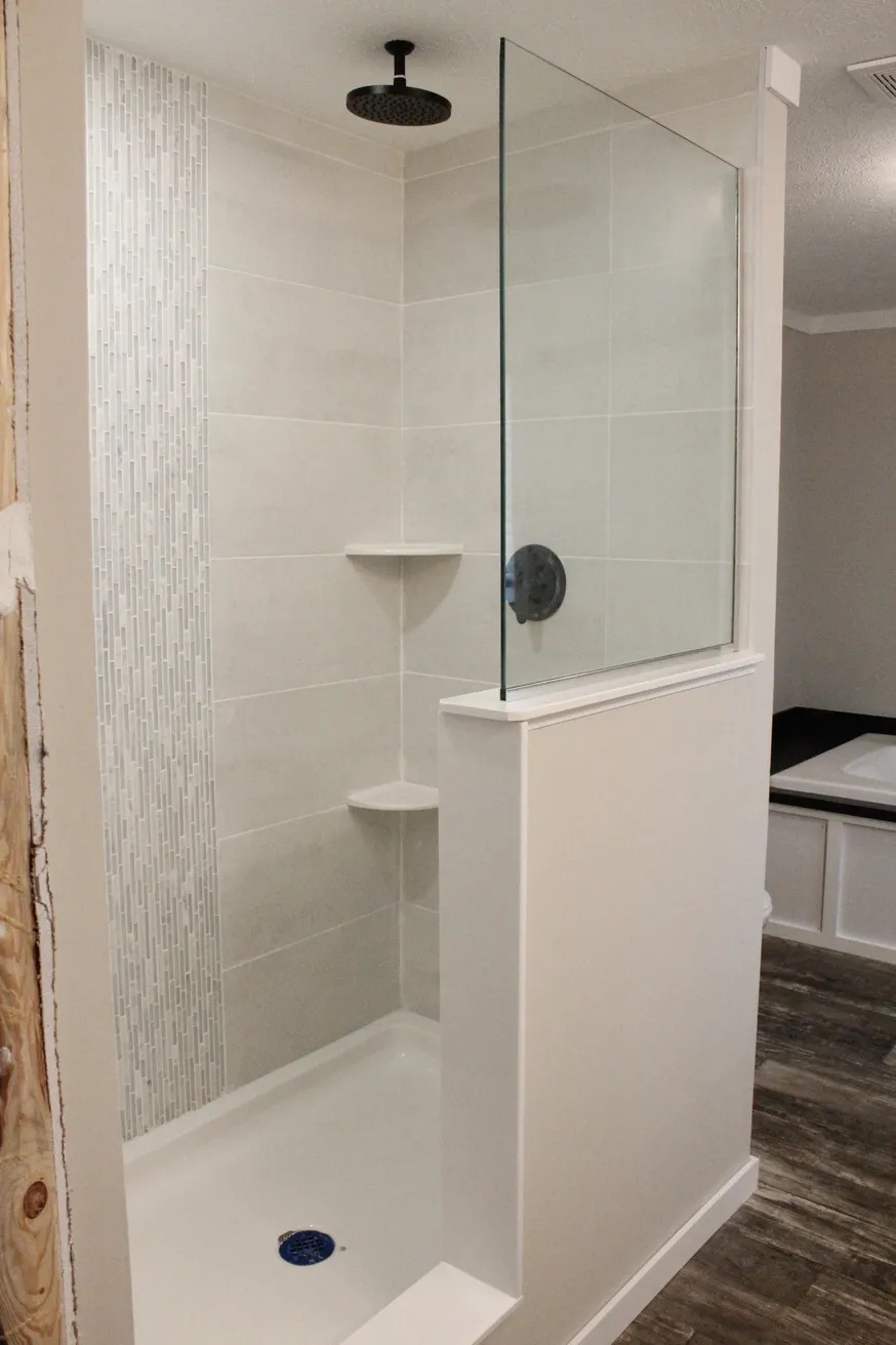 A modern shower with neutral tiles and a vertical accent strip, featuring a rainfall showerhead and glass partition. Minimalist and clean design.