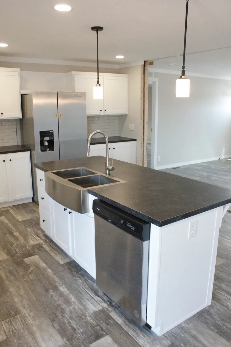 Modern kitchen with a black countertop island, stainless steel sink, and dishwasher. White cabinets, gray tile floor, and pendant lights create a sleek look.