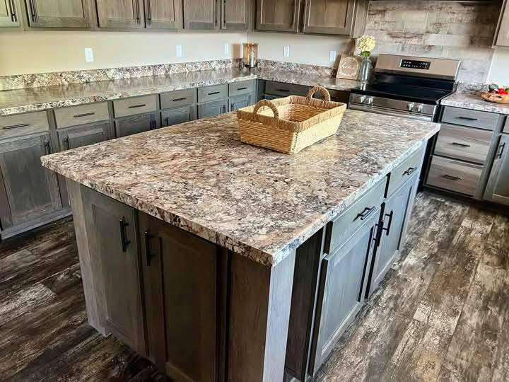 Rustic kitchen with dark wood cabinets and a large granite island featuring a wicker basket. The room has warm lighting and a cozy ambiance.