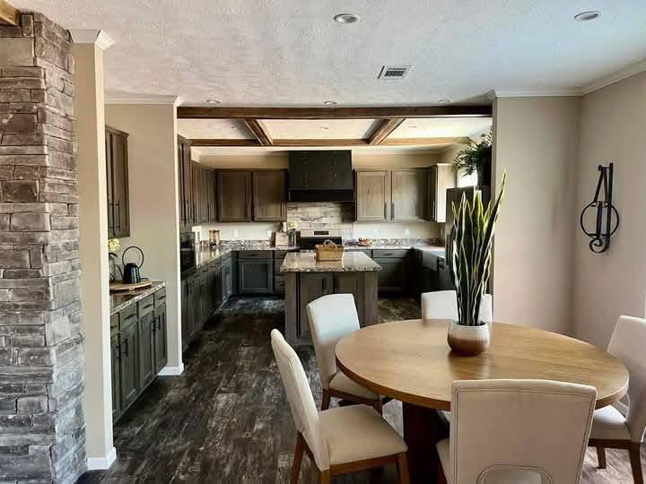 Modern kitchen with dark wood cabinets, stone accent wall, and a dining area with a round wooden table and cream chairs. Potted plant adds greenery. Cozy and inviting atmosphere.