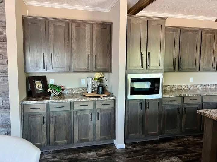 Kitchen with dark wooden cabinets, granite countertops, and a wall-mounted microwave. Decor includes a framed photo, plants, and a coffee maker, creating a cozy and inviting atmosphere.