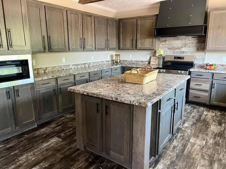 A modern kitchen with dark wood cabinets and granite countertops. A large island with a basket centerpiece is in the center. The atmosphere is warm and inviting.
