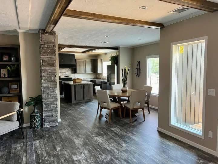 Bright, modern kitchen and dining area with exposed wooden beams. Features include a round table, stone pillar, and large window. Cozy and inviting.