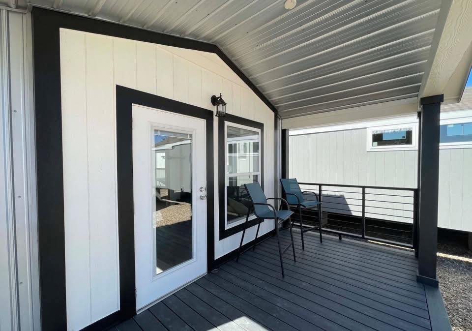 Covered porch with modern black and white siding. Two tall chairs sit near a railing. A glass door and large window add a clean, inviting look.