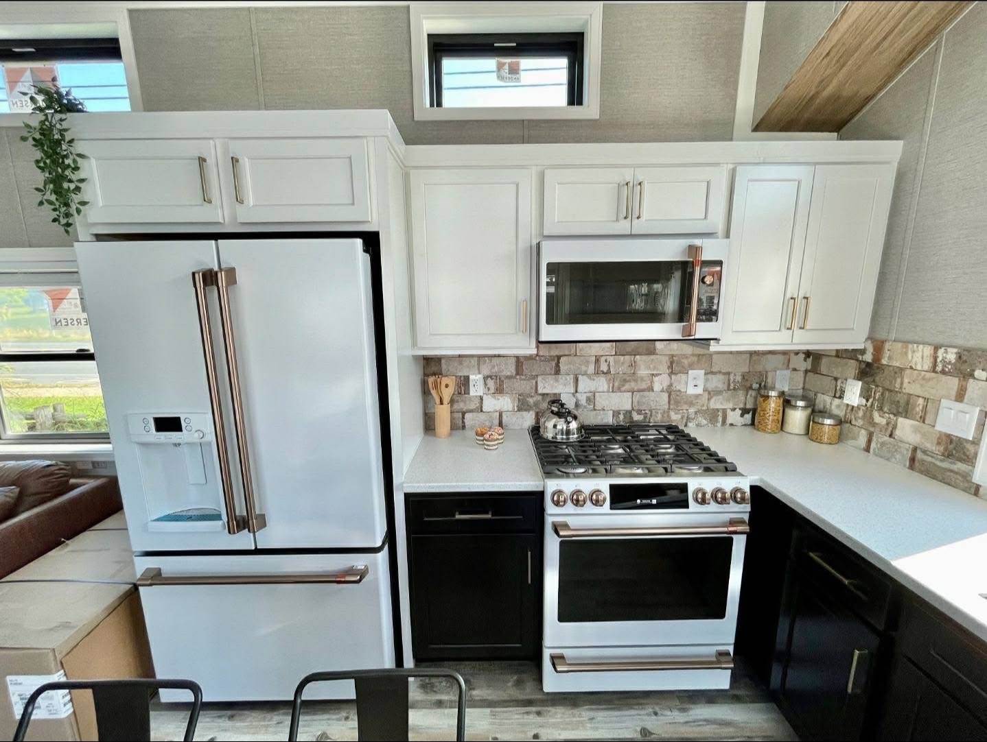 Modern kitchen with white cabinets, stainless steel appliances, and a brick backsplash. Features a fridge, stove, microwave, and countertop jars.