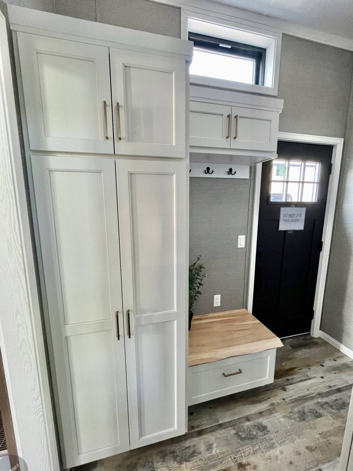 Entryway with white cabinets and natural wood bench beneath hooks, next to a black door. Cozy and organized atmosphere. Gray textured walls.