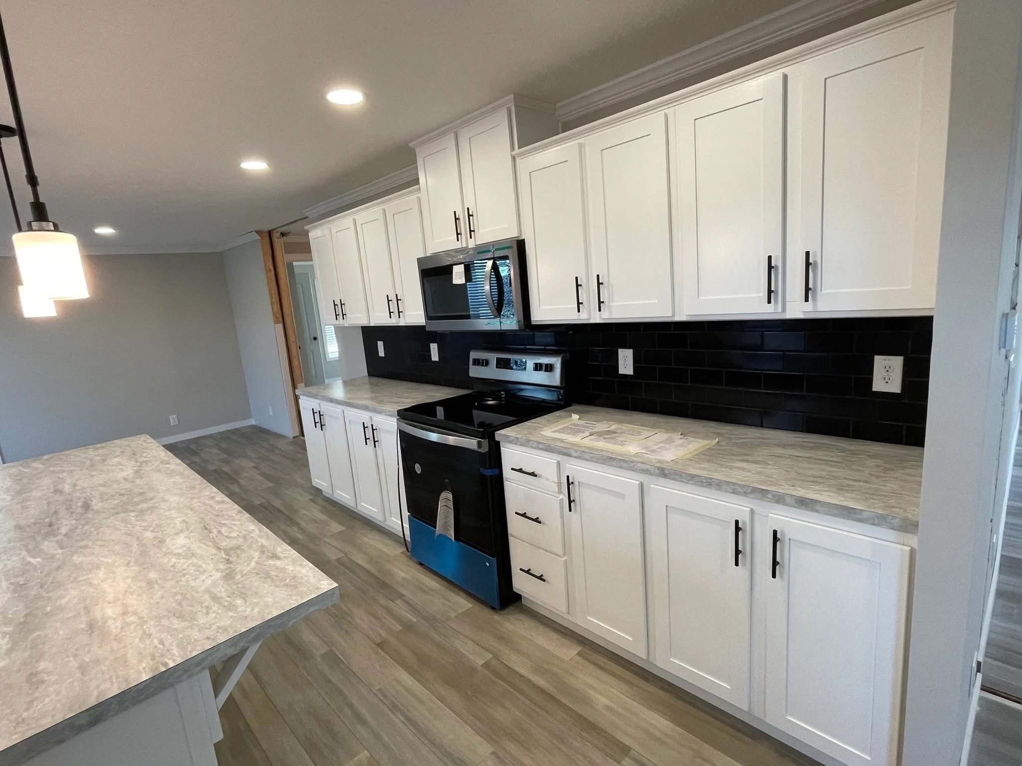 Modern kitchen with white cabinets, black tile backsplash, and gray countertops. Stainless steel appliances and bright lighting convey a clean, inviting feel.