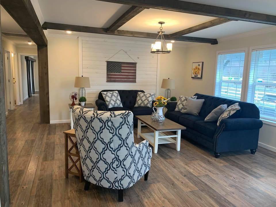 A cozy living room with wooden floors, a patterned armchair, and two navy sofas. An American flag decorates the wall, exuding a warm, inviting tone.