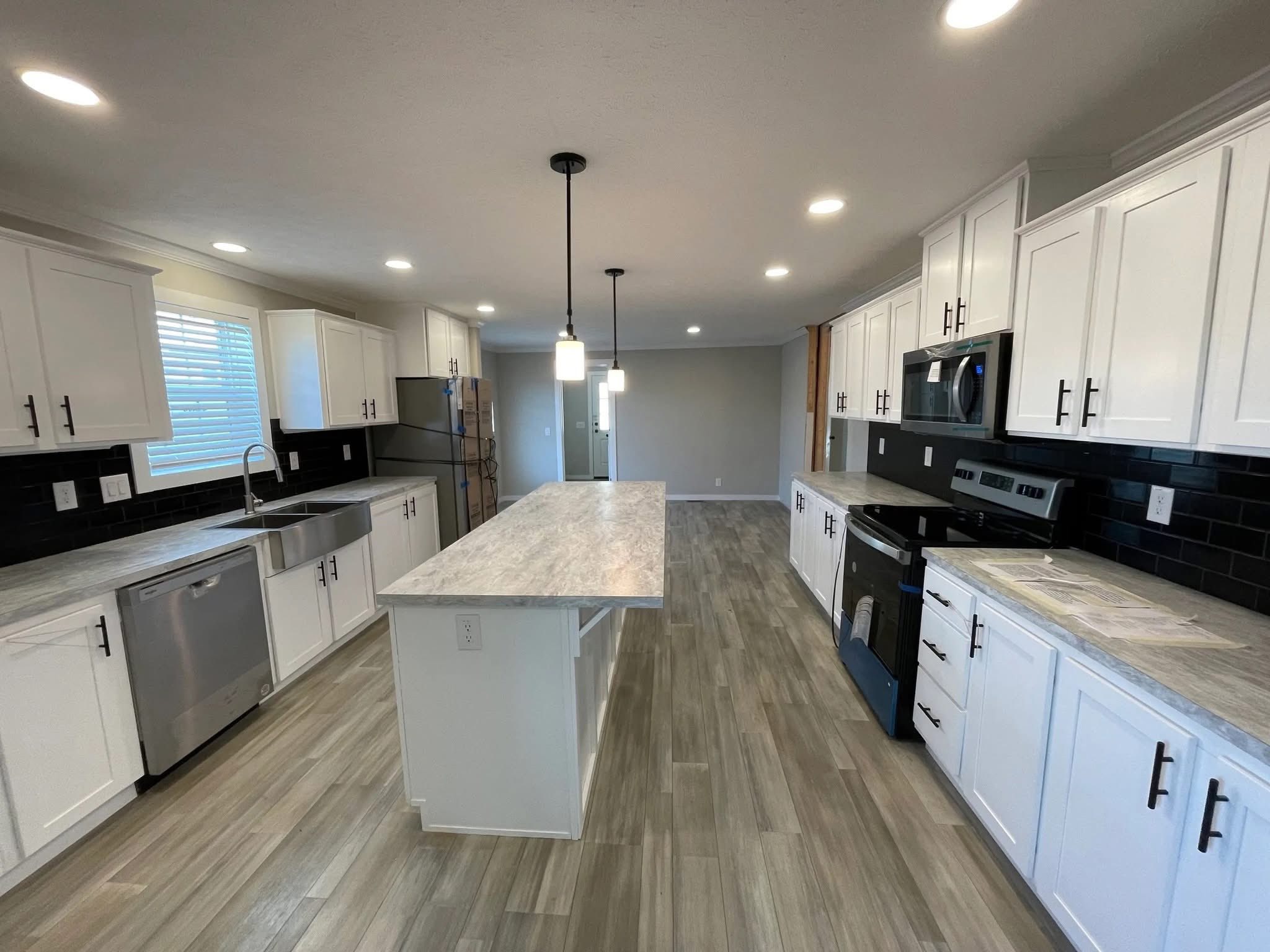 Spacious modern kitchen with white cabinets, black hardware, stainless steel appliances, and pendant lights over a central island on wood-patterned floor.