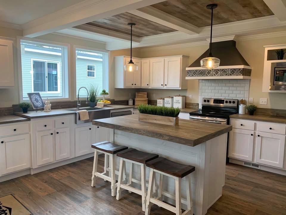 Modern kitchen with white cabinets, wooden countertops, and a central island with stools. Pendant lights hang above, creating a warm, inviting atmosphere.
